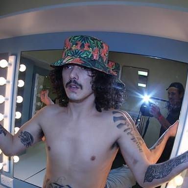 a shirtless man with long hair and tattoos is taking a selfie in front of a mirror