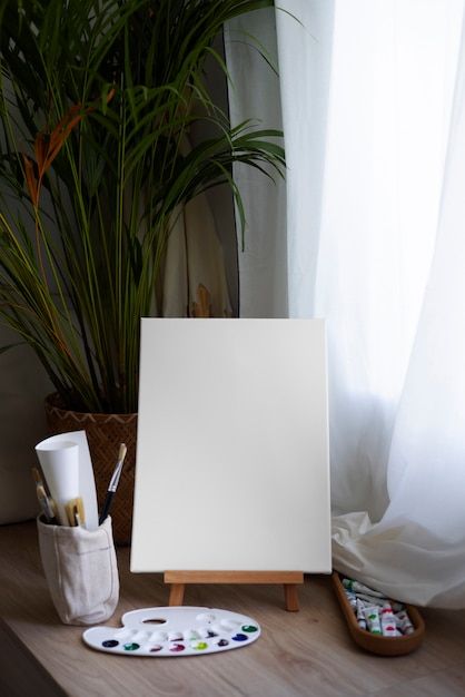 an easel, paintbrushes and other items sit on a table in front of a window