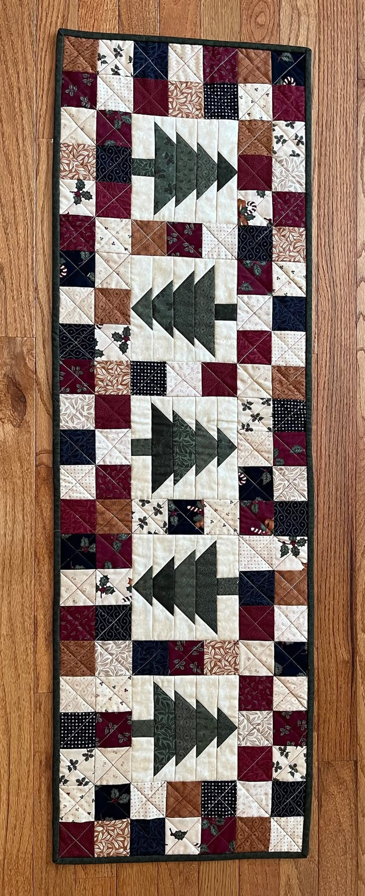 a quilted wall hanging on the side of a wooden floor with an arrow design