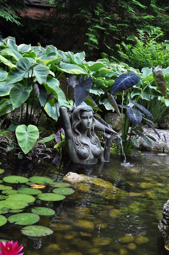 there is a statue in the water surrounded by lily pads and other greenery,