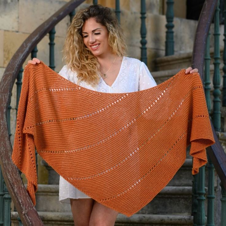 a woman holding up an orange shawl in front of a stair case and railing