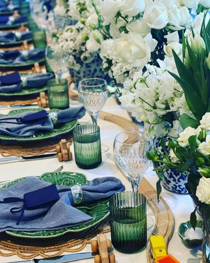 the table is set with blue and white flowers in vases, napkins and glasses