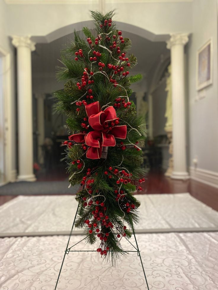 a christmas tree decorated with red bows and berries on a tripod in a hallway