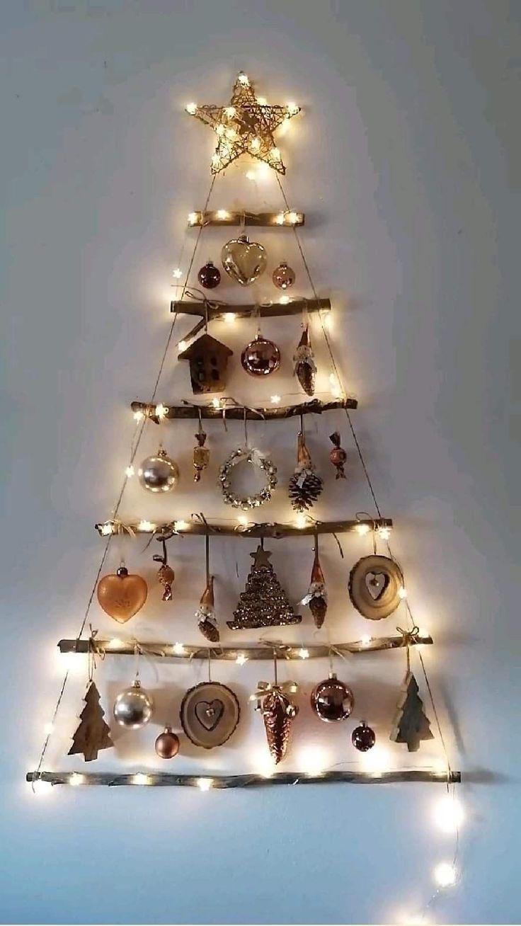 a lighted christmas tree with ornaments and lights on the top, against a white wall