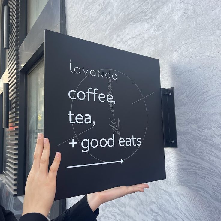 a person holding up a sign that says coffee, tea, and good eats