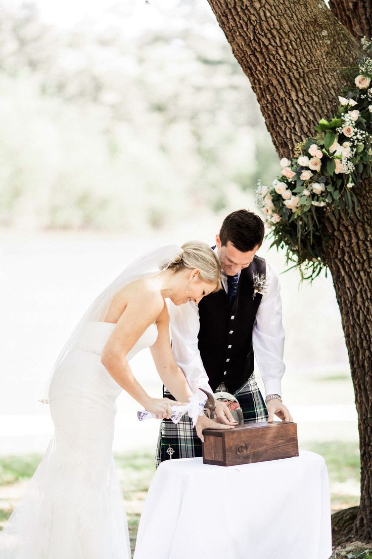 a bride and groom are cutting their wedding cake at the table outside under a tree