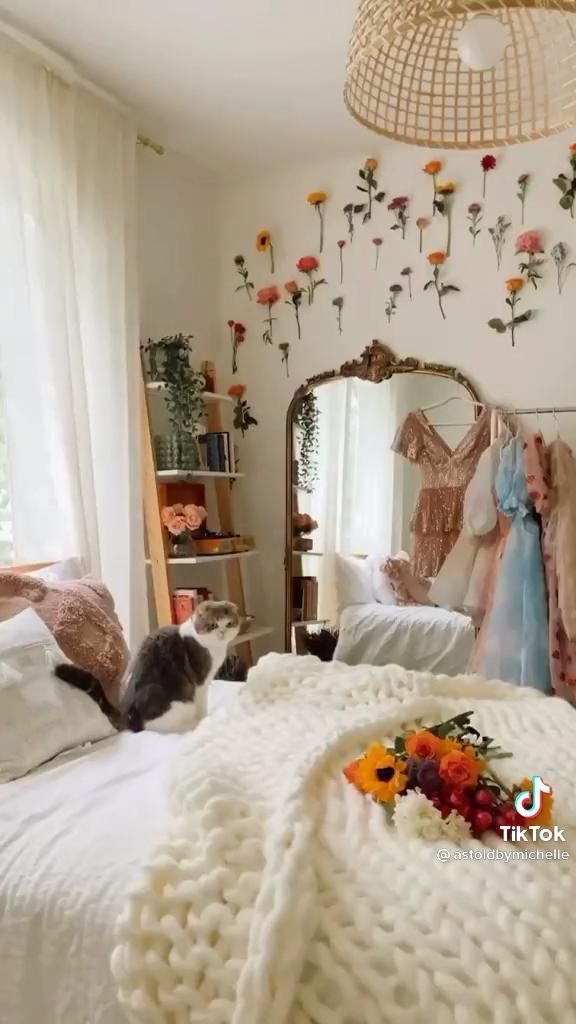 there is a cat laying on the bed in front of a mirror with flowers hanging from it