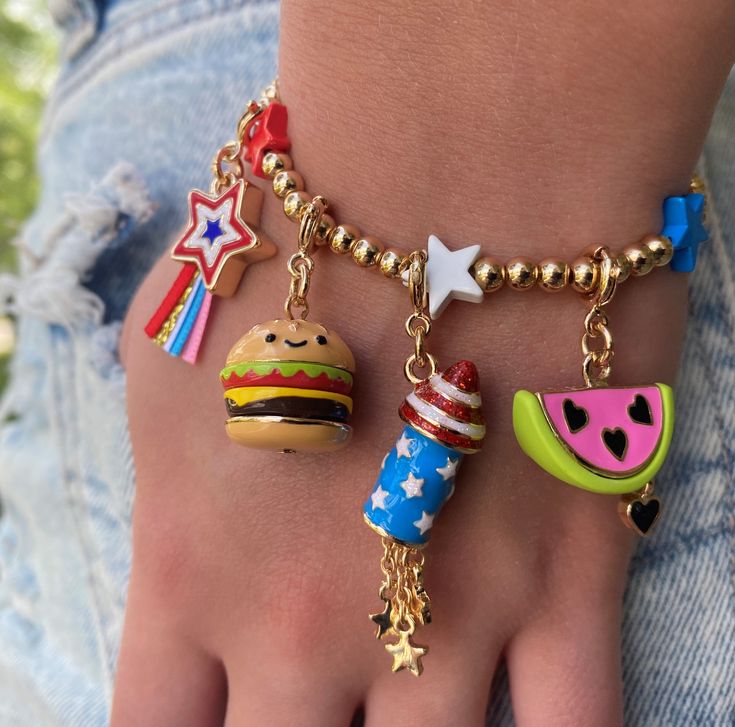 a close up of a person's hand wearing bracelets with food charms on them