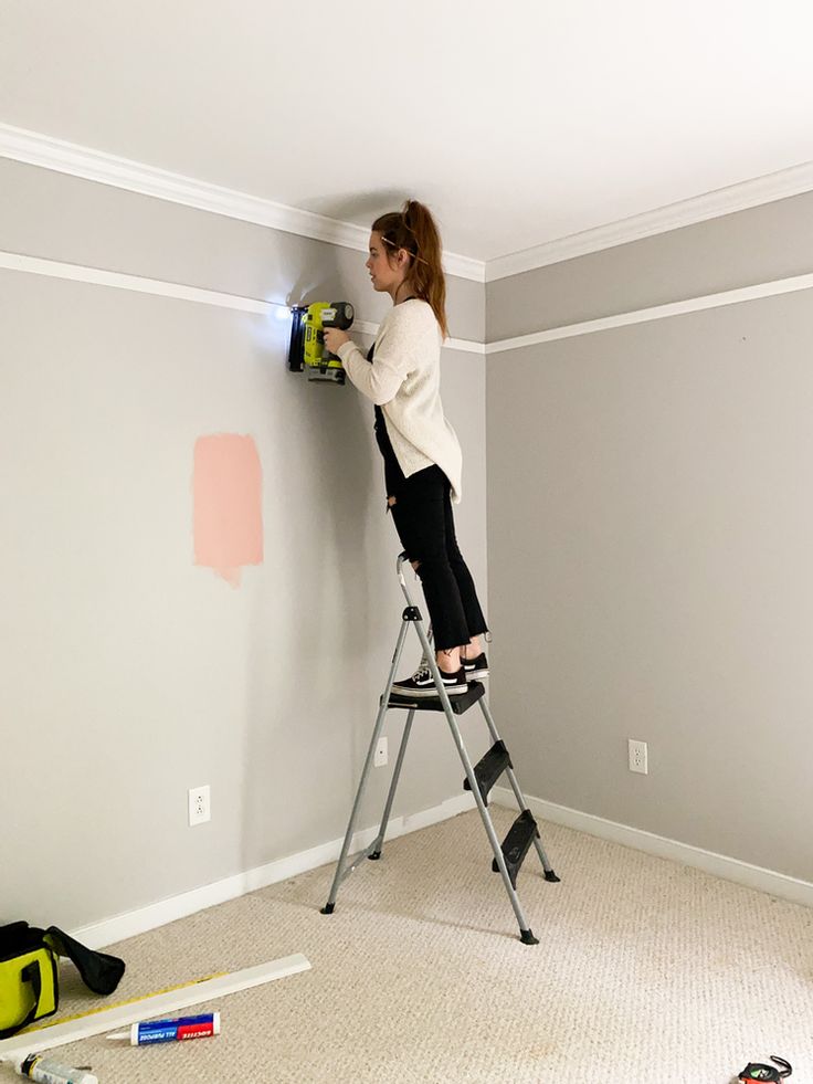 a woman on a ladder painting the wall with paint rollers and an electric drill