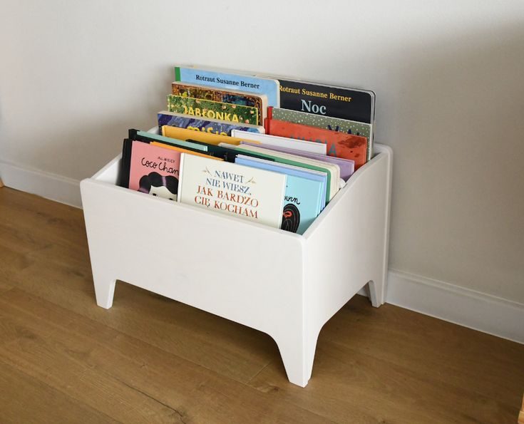 there is a white book stand with books in it on the floor next to a wall