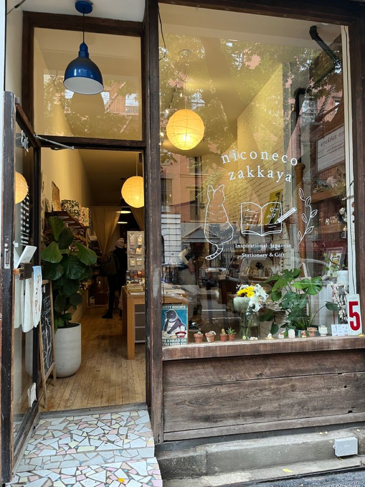 the front window of a flower shop with potted plants and lights hanging from it's windows