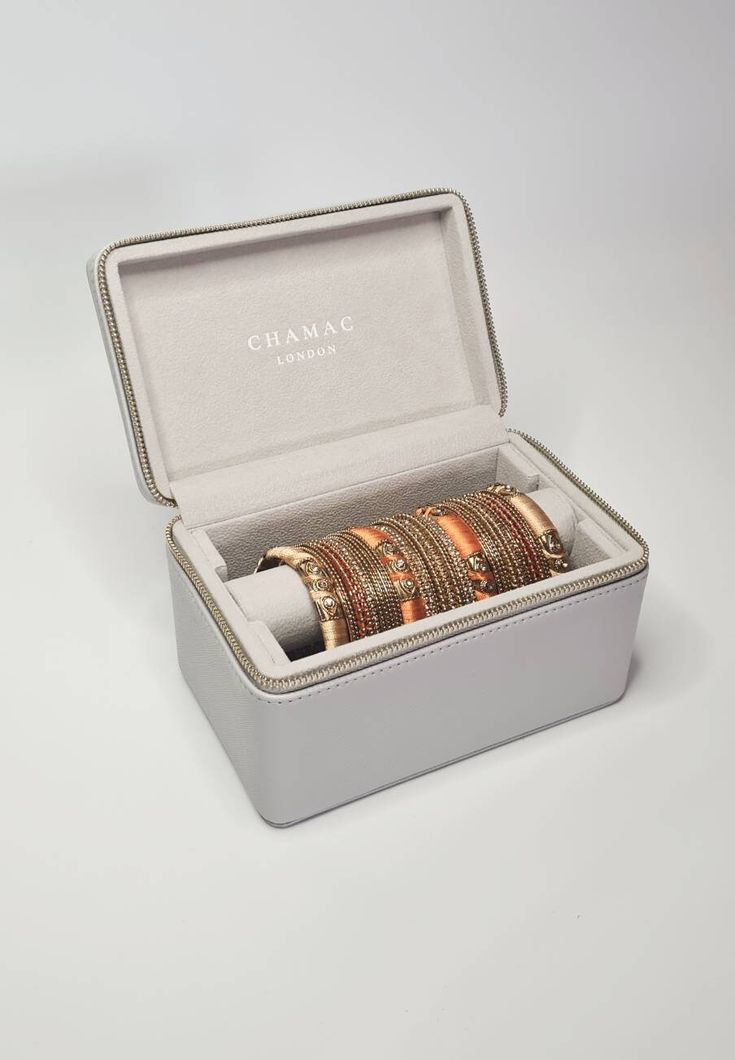 an open box with five gold bracelets inside on a white surface, the lid is closed