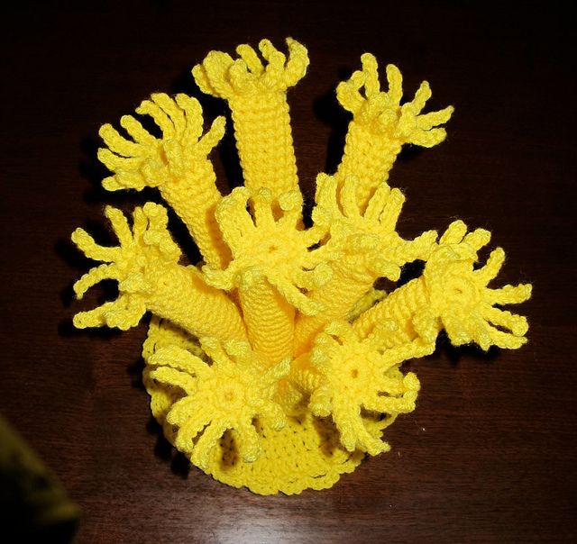 a crocheted yellow coral on a wooden table with a black object in the background