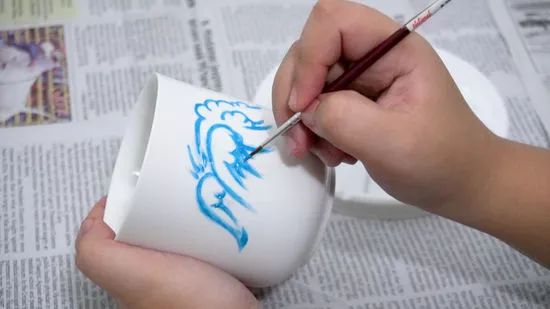 someone is drawing on a coffee cup with blue ink