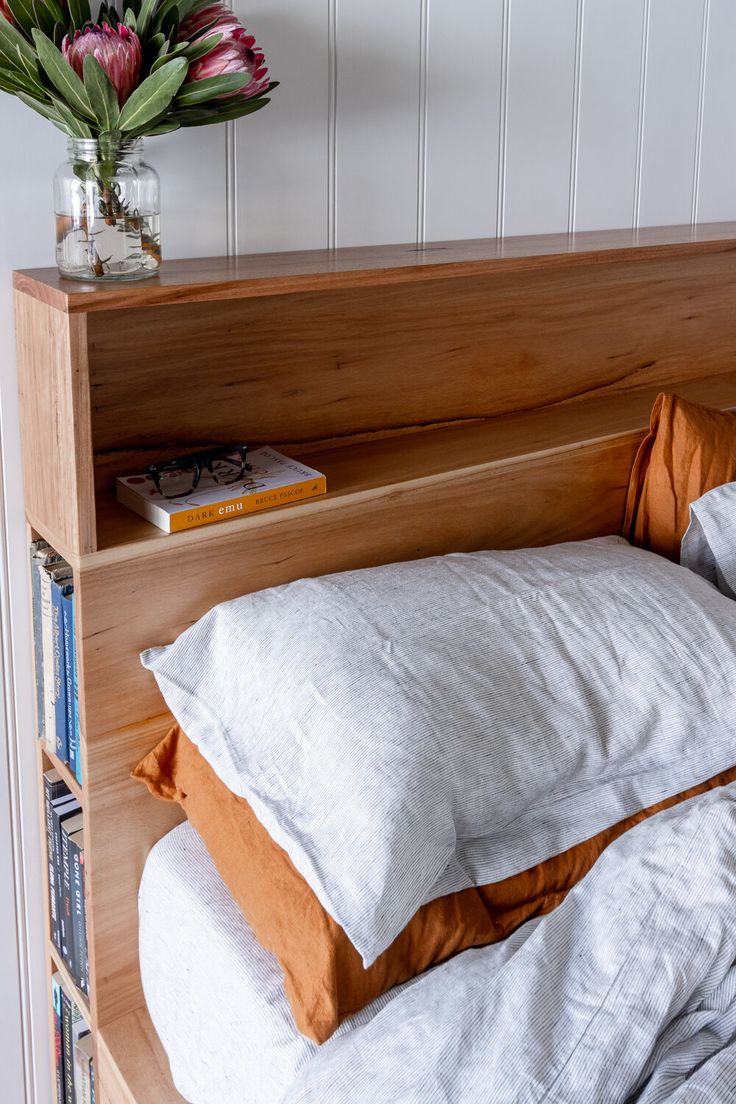 a bed with two pillows on it next to a book shelf and flowers in a vase