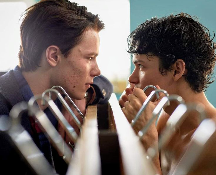 two young men sitting next to each other in front of metal railings and looking at each other