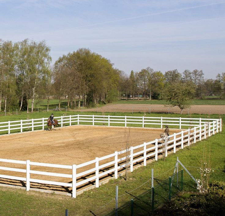 a person riding a horse in an enclosed area with white fence and green grass on the other side