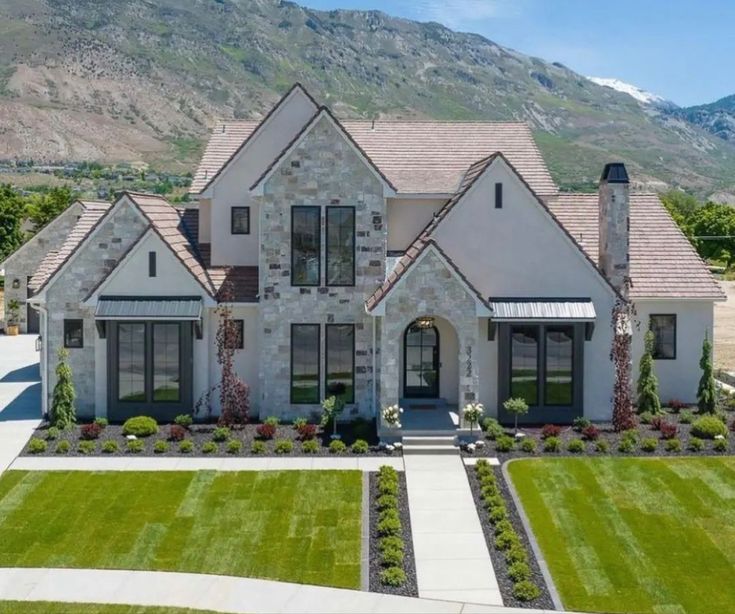 a large white house in the middle of a field with mountains in the back ground