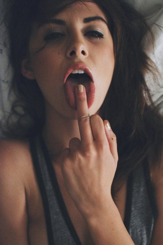 a woman laying in bed with her finger on her mouth and tongue out to the side