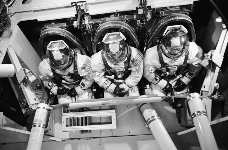 three men in space suits and helmets are sitting on the back of a vehicle with pipes