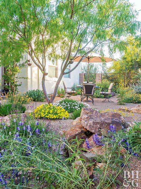 a garden with rocks and flowers in the foreground, an outdoor dining area on the other side