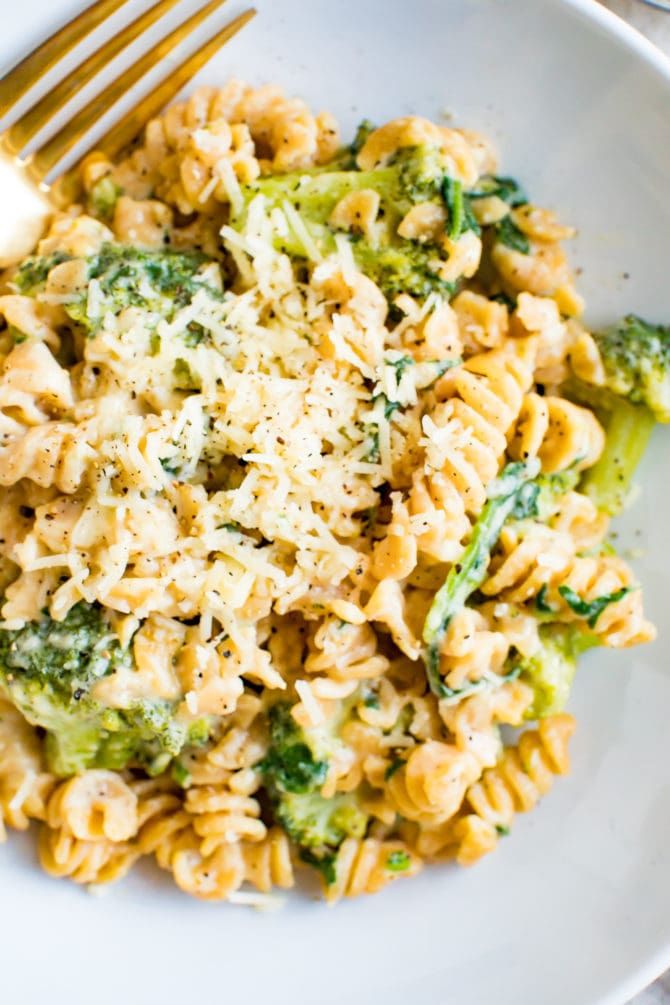 a white plate topped with pasta and broccoli covered in parmesan cheese