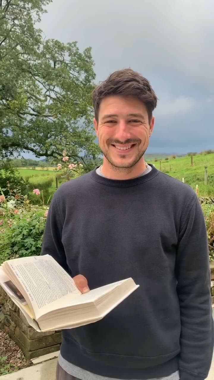 a man is holding an open book in his right hand and smiling at the camera