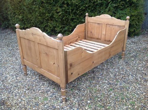 a wooden bed frame sitting on top of gravel covered ground next to a green bush