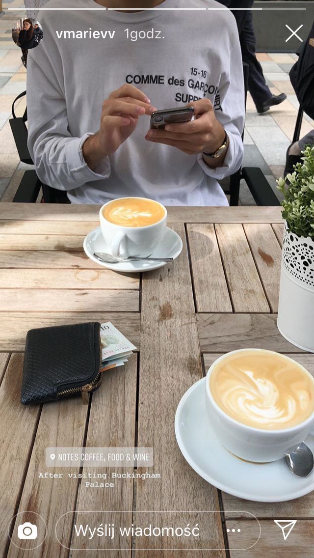 a man sitting at a table with two cups of coffee in front of him while looking at his cell phone