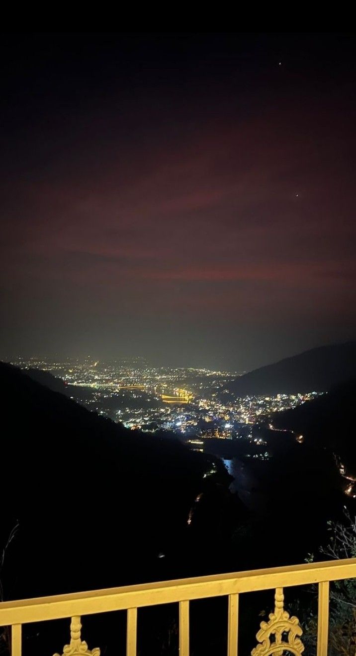 the city lights are lit up in the night sky from atop a hill overlooking a valley