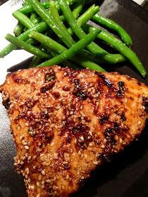 a piece of meat and some green beans on a black plate with a fork next to it