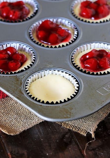 muffin tins filled with cupcake batter and topped with fresh cherries on a wooden table