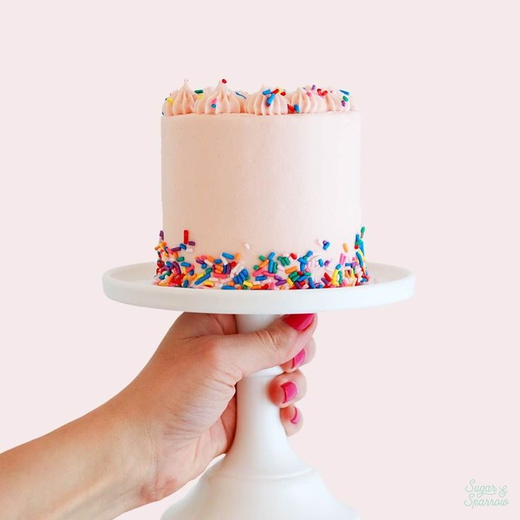 a hand holding a cake with sprinkles on it and a white plate