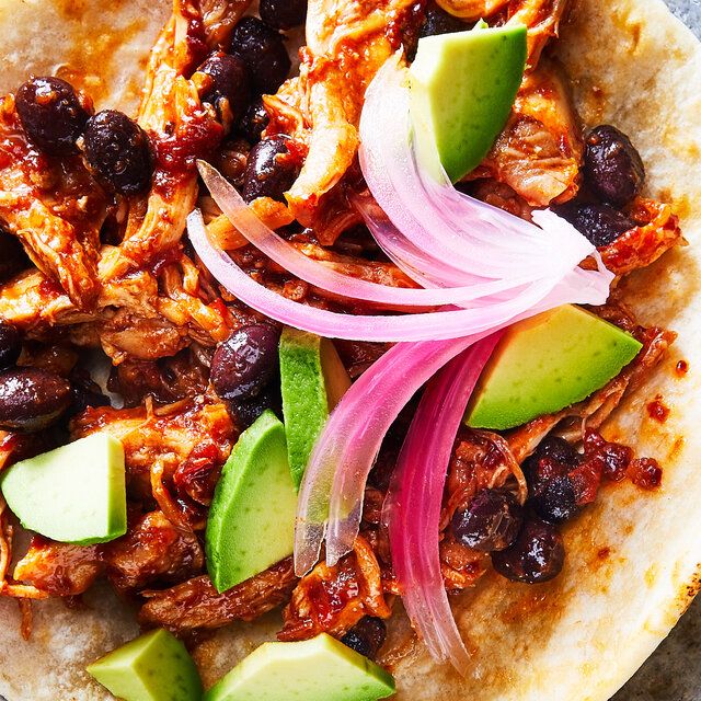 a tortilla topped with meat, onions and avocado