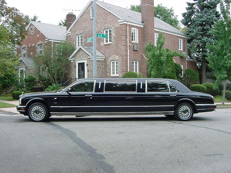 a black limousine is parked in front of a large brick house on a street corner