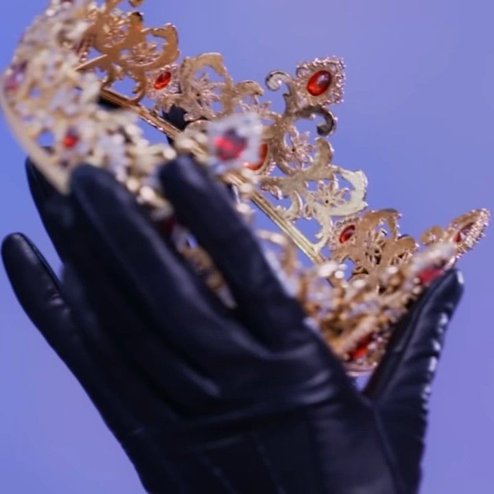 a hand wearing black gloves holding a gold tiara