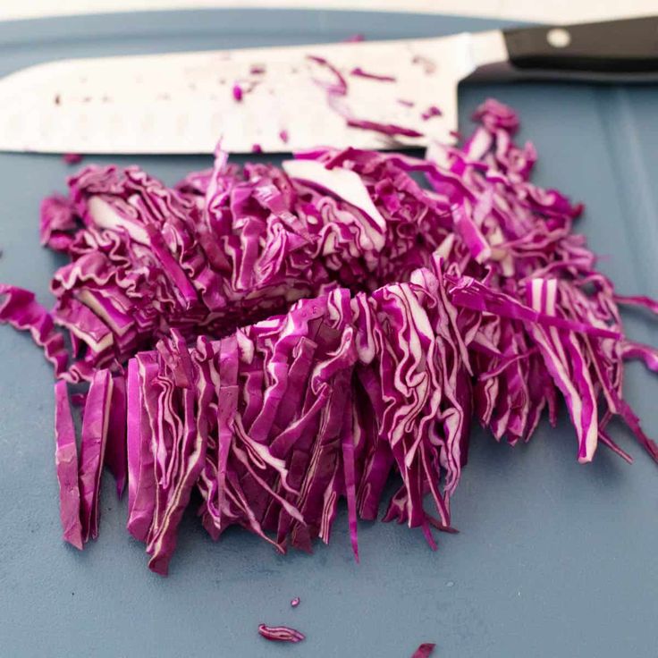 chopped red cabbage sitting on top of a cutting board next to a knife