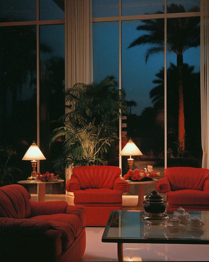 a living room filled with red couches next to tall windows and palm trees in the background