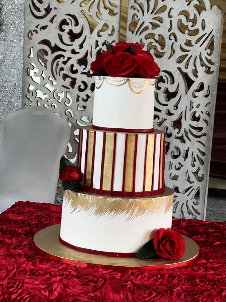 a three tiered wedding cake with red roses on the top and gold trimmings