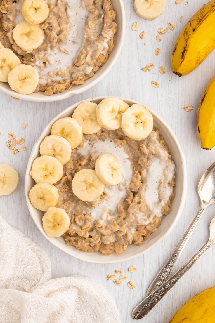 two bowls filled with oatmeal and bananas on top of a white table