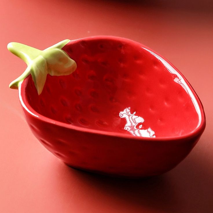 a red bowl sitting on top of a table with a green plant in the middle