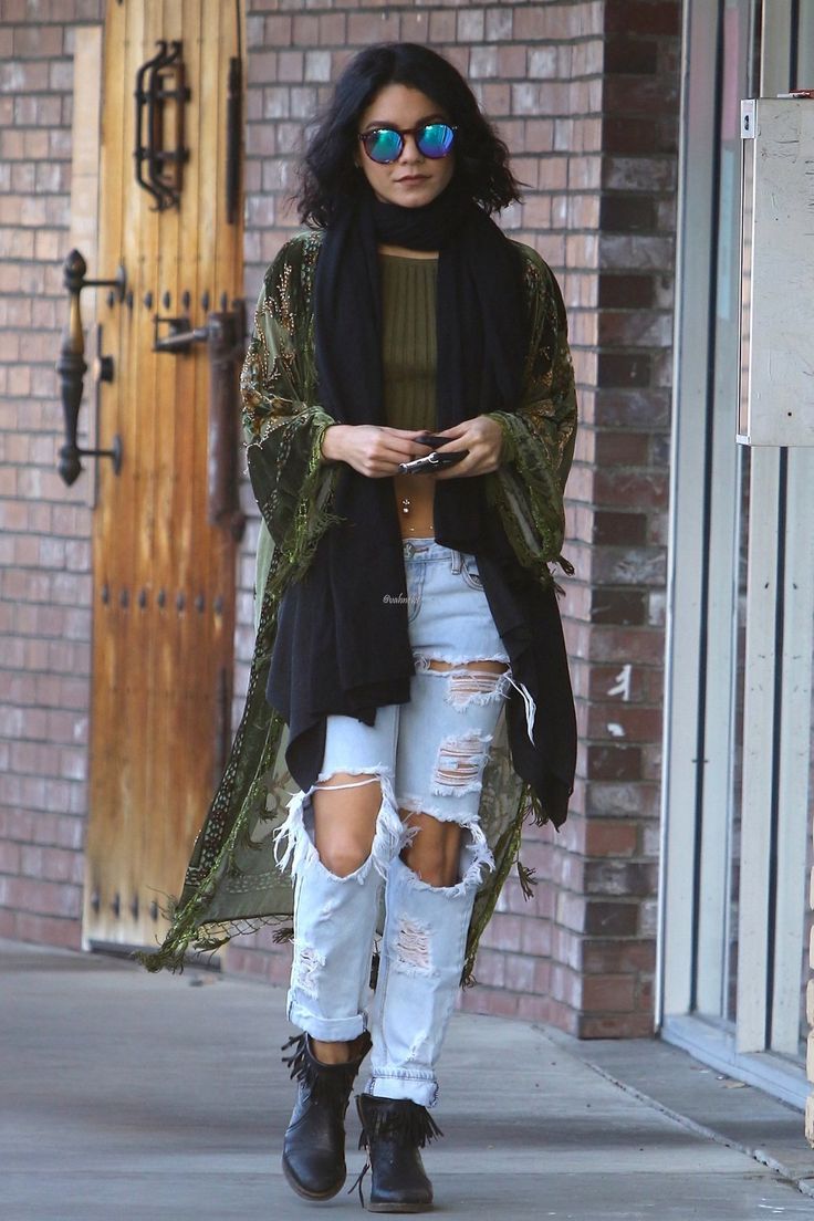 a woman in ripped jeans and black boots is looking at her cell phone while walking down the street