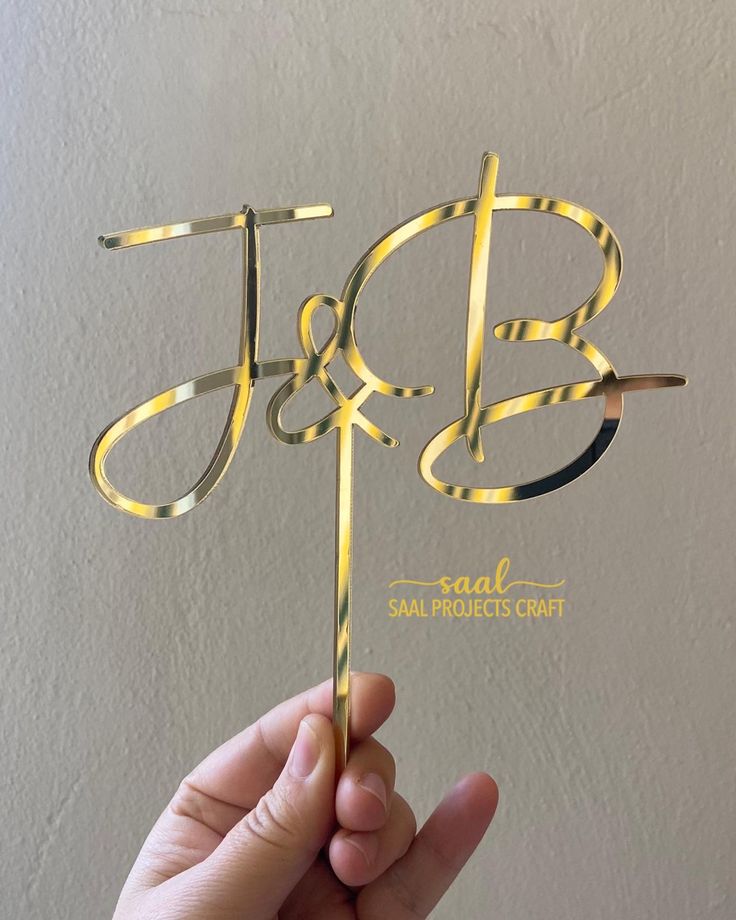 a hand holding up a cake topper with the letter j and b on it