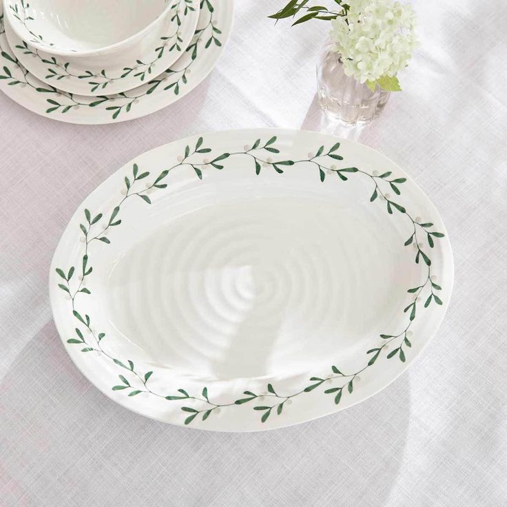 two white plates with green leaves on them sitting on a table next to a flower vase