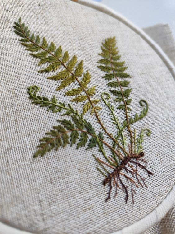 a close up of a embroidery on a white hoop with green leaves and roots in it