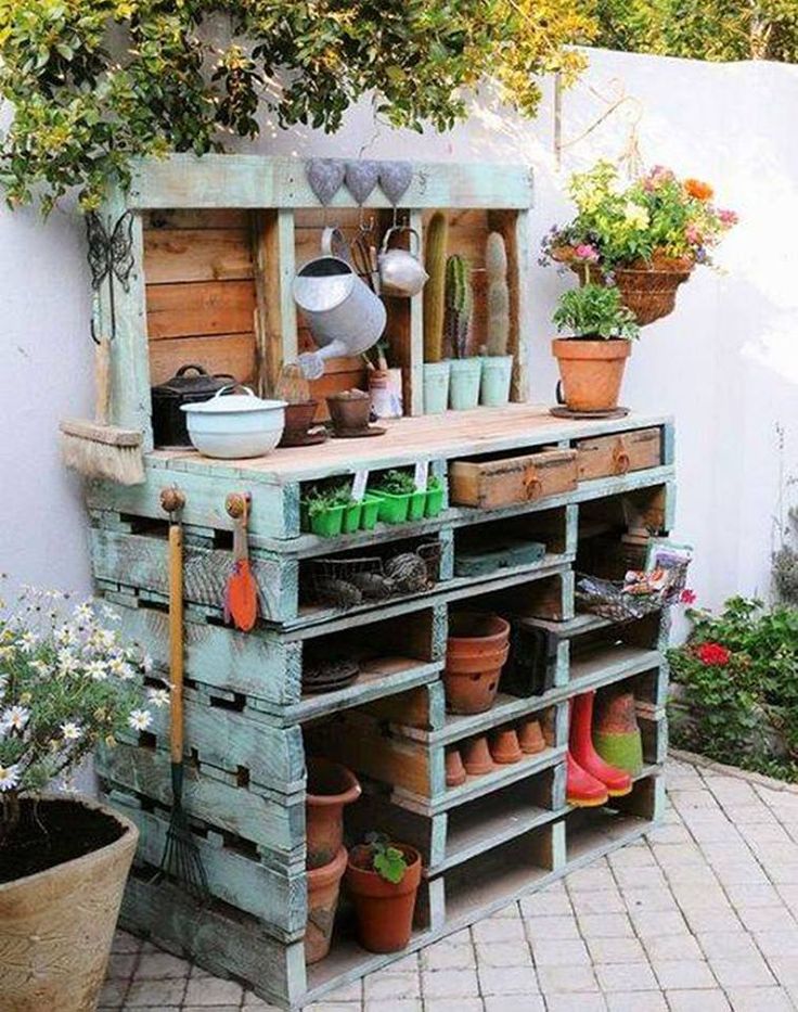 an outdoor garden area with potted plants and pots on the shelf, in front of a white fence