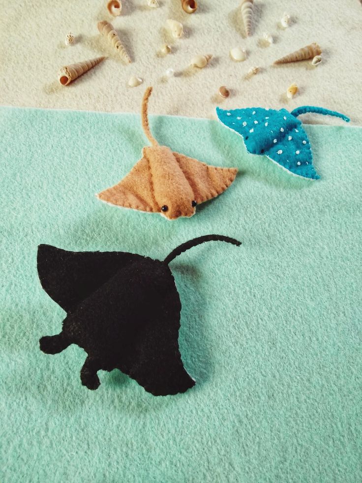 three felt animals are laying on a blue towel next to shells and seashells