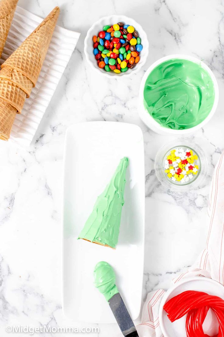 green frosted christmas tree on a white plate next to bowls of candy and an ice cream cone