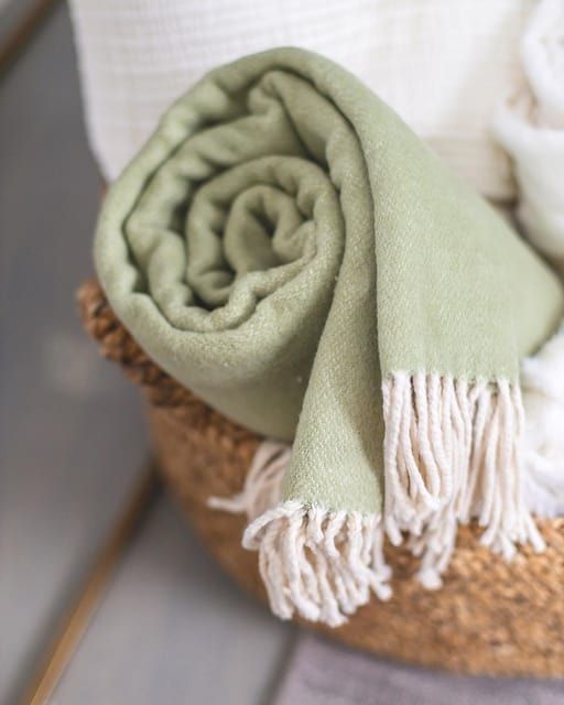 a green and white blanket sitting on top of a woven basket next to folded towels