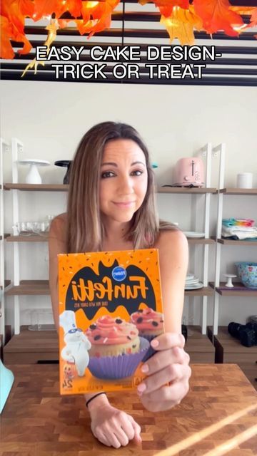 a woman sitting at a table holding up a box of funfetti cupcakes